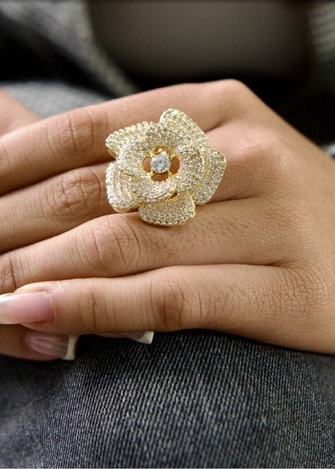 Anillo dorado con forma de flor y brillo, puesto en la mano