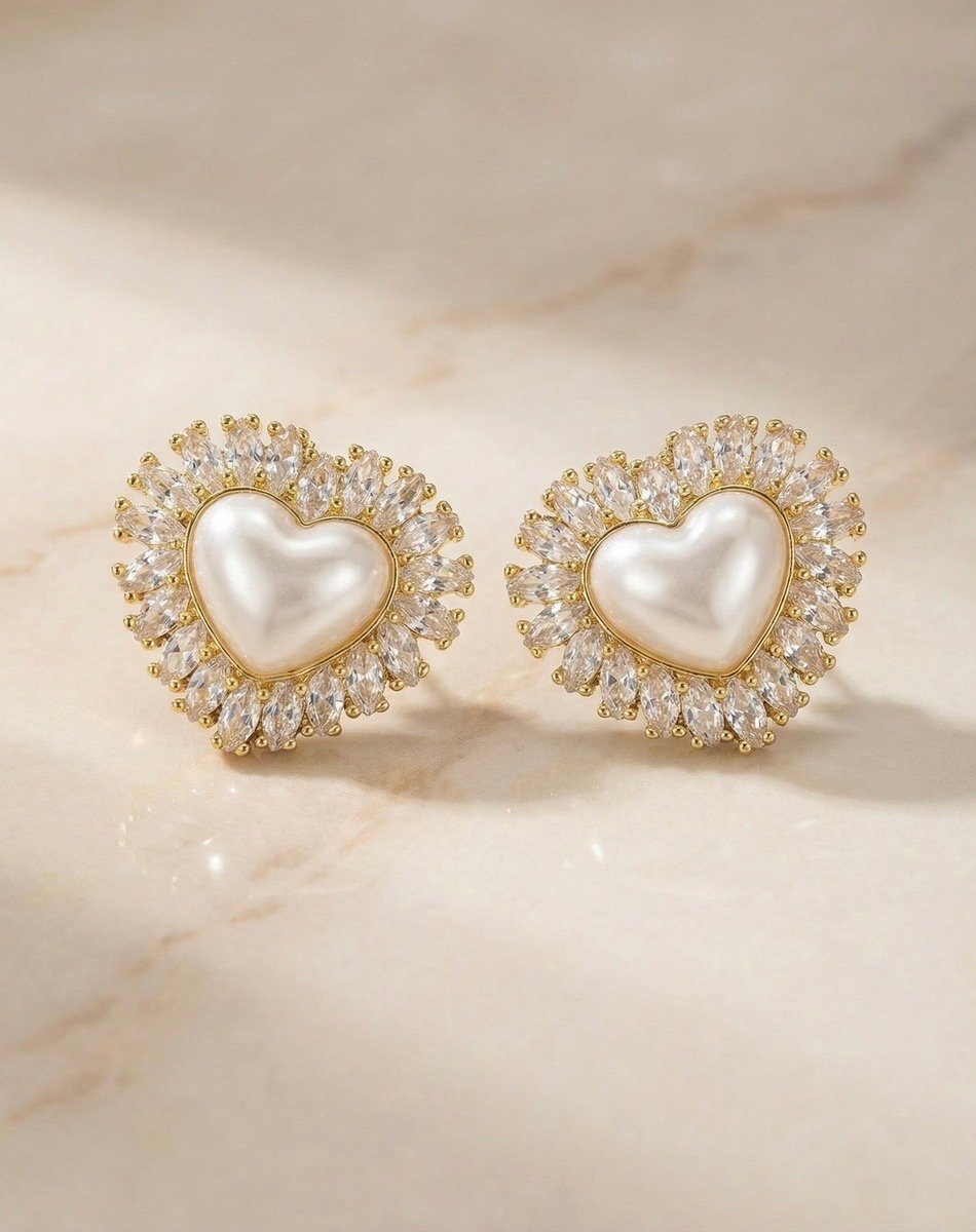 Aretes de corazón con perla y borde de brillo sobre superficie clara