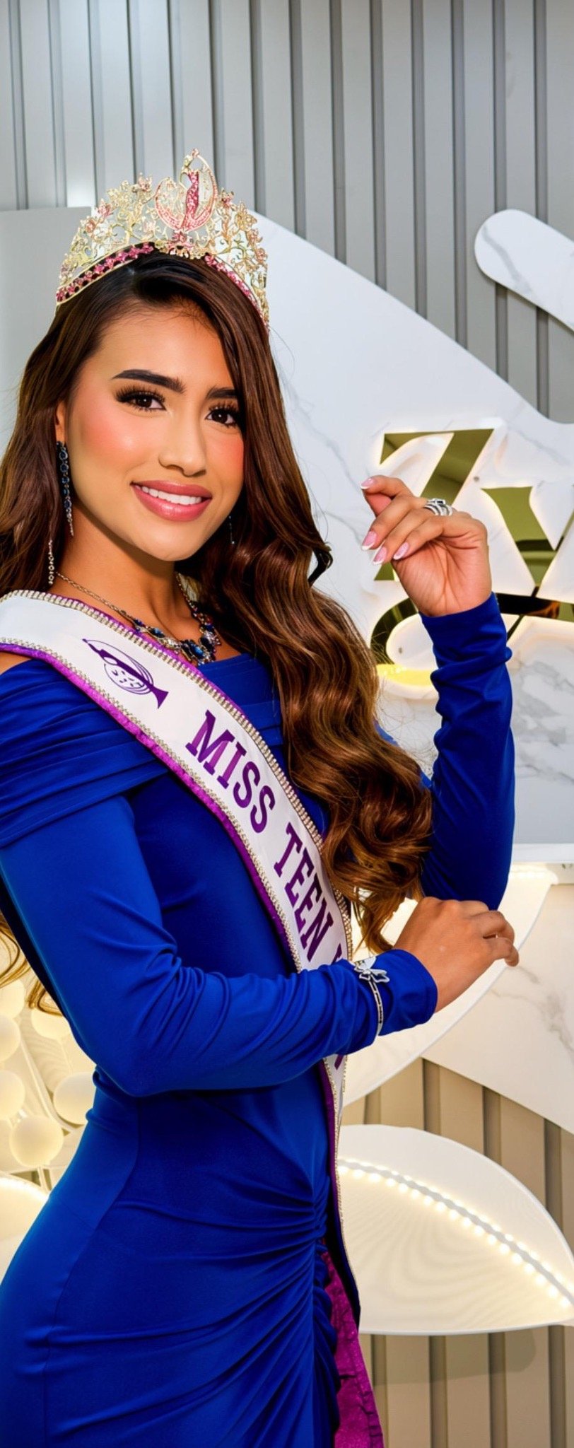 Participante con corona y banda, con vestido azul, frente al logo ZYRAL
